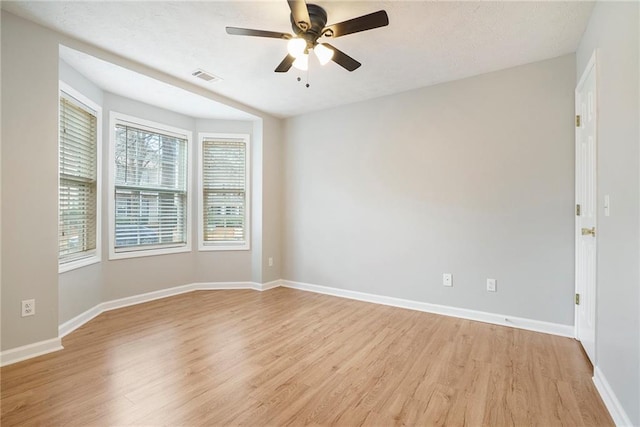 spare room featuring light wood finished floors, visible vents, a ceiling fan, a textured ceiling, and baseboards