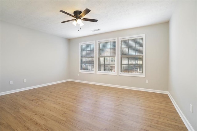 empty room with a textured ceiling, light wood-type flooring, visible vents, and baseboards