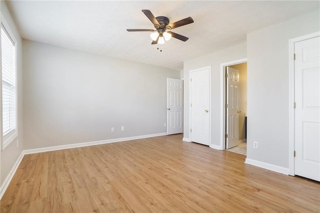 unfurnished bedroom with a ceiling fan, baseboards, multiple windows, and light wood finished floors