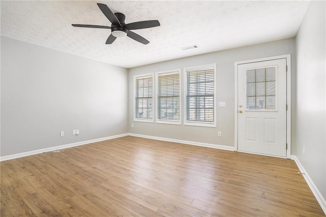 interior space featuring light wood-type flooring, visible vents, a textured ceiling, and baseboards