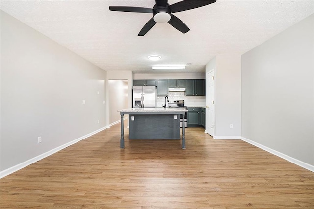 kitchen with stainless steel appliances, light countertops, light wood-style floors, under cabinet range hood, and a kitchen bar