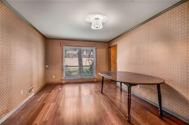 unfurnished dining area featuring visible vents, wallpapered walls, baseboards, ornamental molding, and wood finished floors