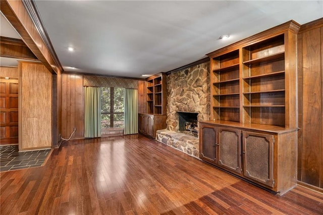 unfurnished living room featuring wooden walls, built in shelves, crown molding, a fireplace, and dark wood-style floors