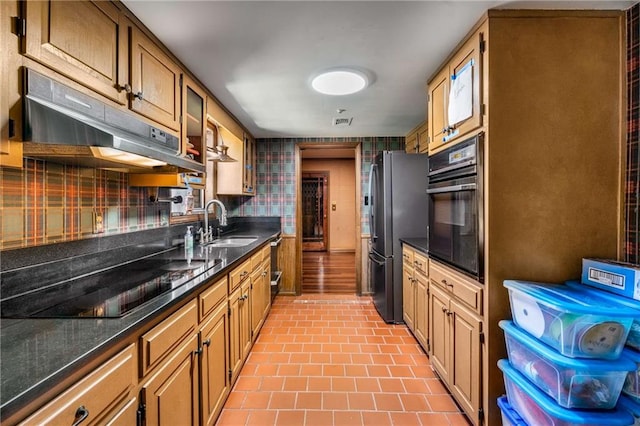 kitchen with glass insert cabinets, under cabinet range hood, decorative backsplash, black appliances, and a sink