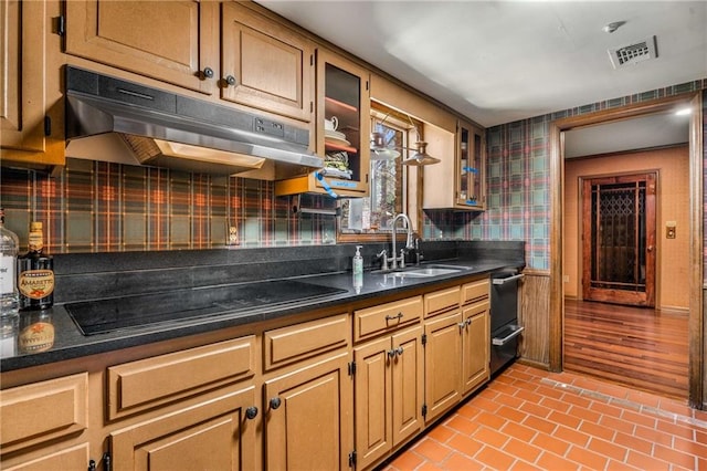 kitchen featuring visible vents, black electric stovetop, under cabinet range hood, brick floor, and a sink