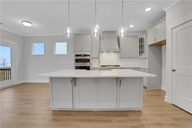 kitchen featuring an island with sink, custom range hood, pendant lighting, and double oven