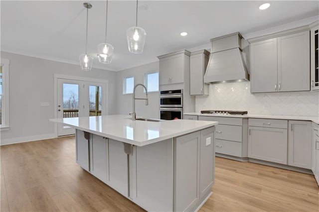 kitchen featuring sink, gray cabinets, a kitchen island with sink, hanging light fixtures, and custom exhaust hood