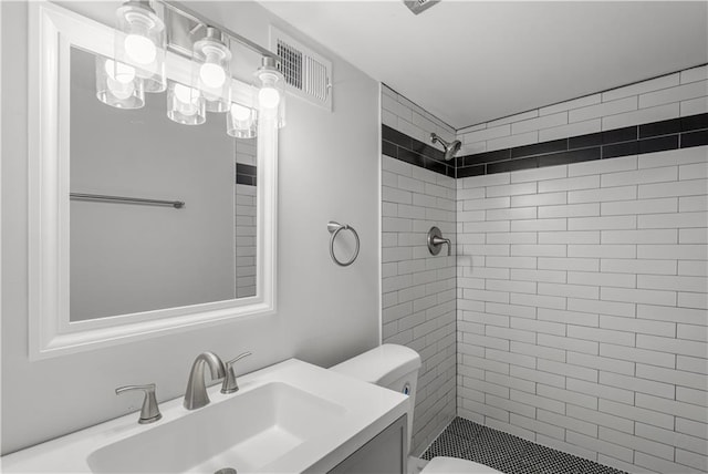 bathroom featuring tiled shower, vanity, and toilet