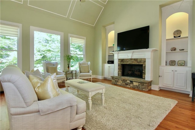 living room featuring vaulted ceiling, a stone fireplace, built in shelves, and light hardwood / wood-style floors