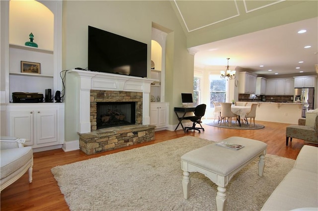 living room featuring a stone fireplace, lofted ceiling, light hardwood / wood-style flooring, a chandelier, and built in shelves