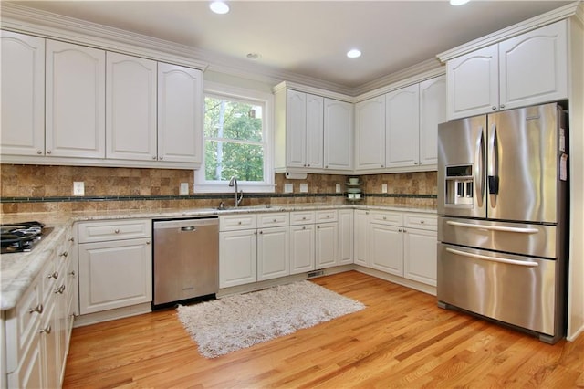 kitchen with appliances with stainless steel finishes, crown molding, white cabinets, and light wood-type flooring