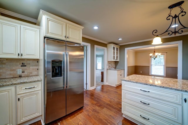 kitchen featuring stainless steel fridge, light wood-style flooring, glass insert cabinets, light stone counters, and hanging light fixtures