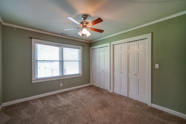 unfurnished bedroom with ornamental molding, carpet flooring, two closets, and visible vents