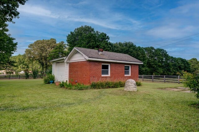 view of side of home featuring an outbuilding, a garage, brick siding, fence, and a lawn