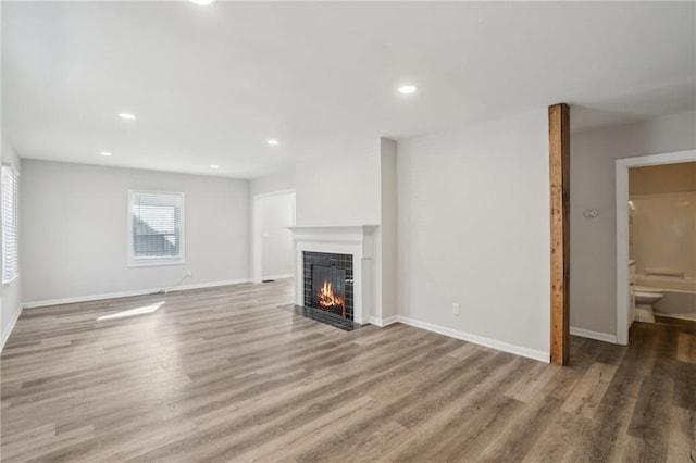 unfurnished living room with wood finished floors, a fireplace with flush hearth, and baseboards