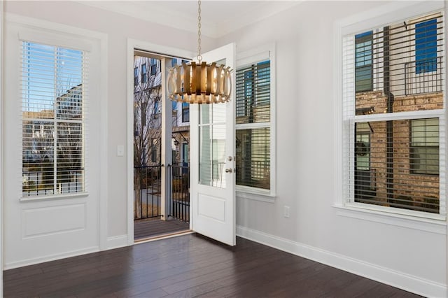 unfurnished dining area with an inviting chandelier, baseboards, dark wood finished floors, and ornamental molding