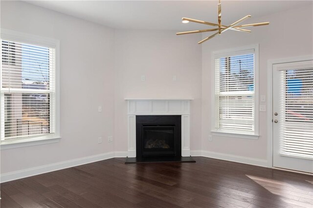 unfurnished living room featuring dark wood-style flooring, a fireplace, plenty of natural light, and an inviting chandelier