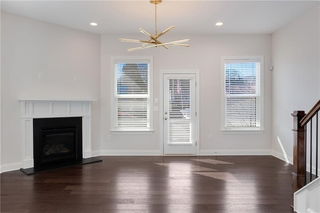 unfurnished living room featuring a fireplace with raised hearth, a chandelier, recessed lighting, stairs, and dark wood finished floors