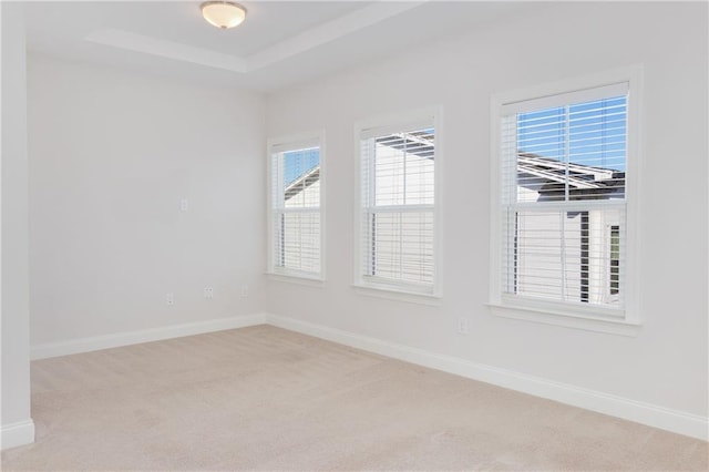 unfurnished room with a tray ceiling, light colored carpet, and baseboards