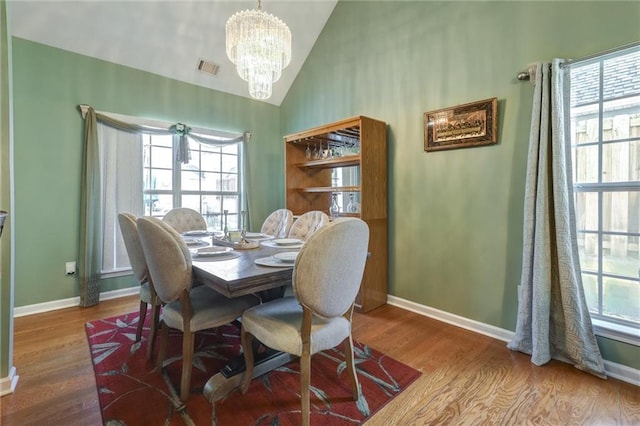 dining space with an inviting chandelier, lofted ceiling, baseboards, and wood finished floors