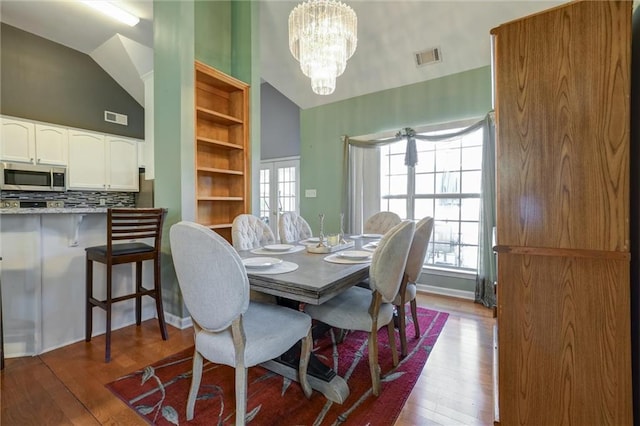 dining space with a chandelier, hardwood / wood-style floors, high vaulted ceiling, and visible vents