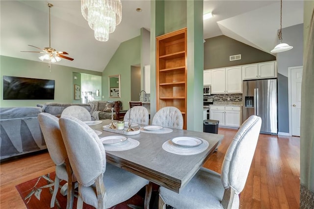 dining area with ceiling fan with notable chandelier, light wood-style flooring, visible vents, and high vaulted ceiling