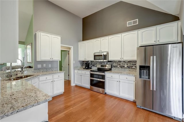 kitchen featuring light stone counters, a sink, white cabinetry, high vaulted ceiling, and appliances with stainless steel finishes