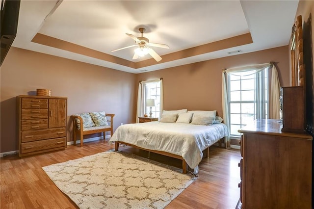 bedroom with a tray ceiling, baseboards, visible vents, and wood finished floors