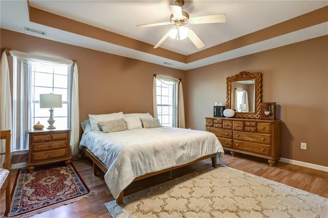 bedroom featuring baseboards, a tray ceiling, visible vents, and wood finished floors