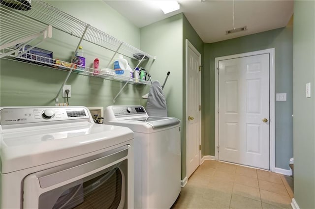 clothes washing area featuring washer and clothes dryer, laundry area, visible vents, light tile patterned floors, and baseboards