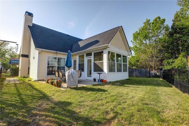 back of property with a chimney, a lawn, a shingled roof, a fenced backyard, and a patio area