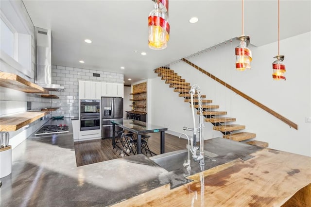 kitchen featuring white cabinetry, hanging light fixtures, wall chimney range hood, stainless steel appliances, and backsplash