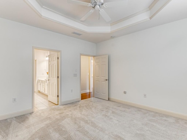 unfurnished bedroom with ceiling fan, crown molding, a tray ceiling, and ensuite bath