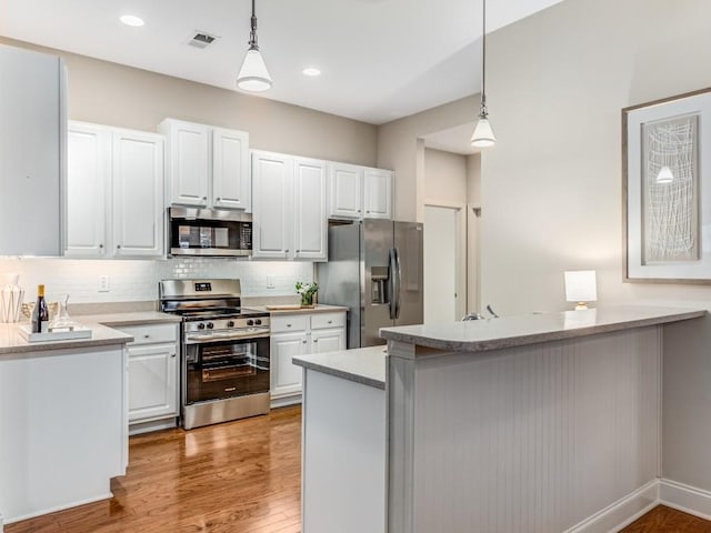 kitchen with light hardwood / wood-style floors, white cabinets, kitchen peninsula, pendant lighting, and stainless steel appliances