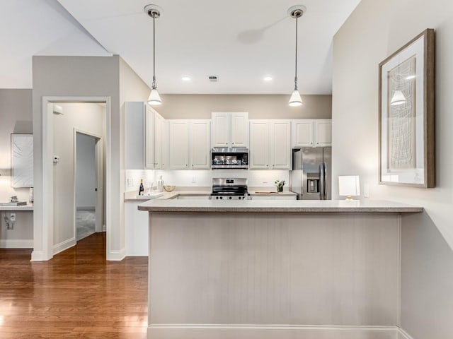 kitchen featuring white cabinets, appliances with stainless steel finishes, dark wood-type flooring, hanging light fixtures, and kitchen peninsula