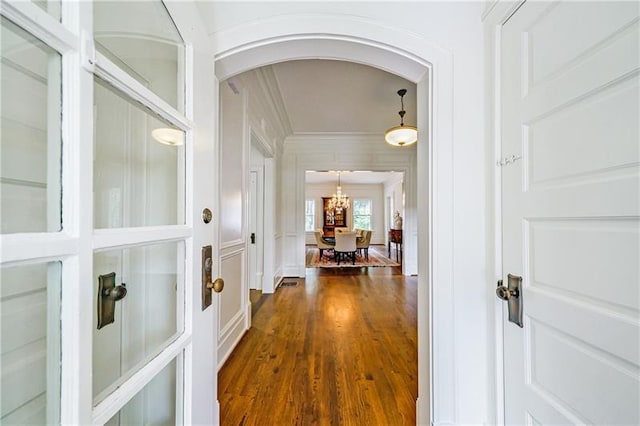 corridor featuring crown molding, an inviting chandelier, and dark hardwood / wood-style flooring