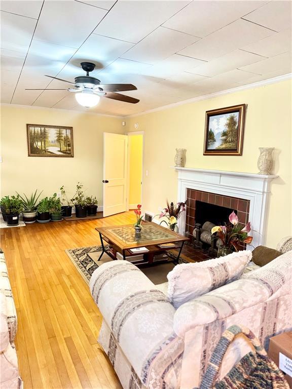 living room with hardwood / wood-style floors, crown molding, a tile fireplace, and ceiling fan