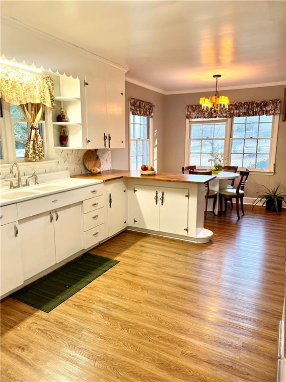 kitchen featuring hanging light fixtures, white cabinetry, ornamental molding, and kitchen peninsula