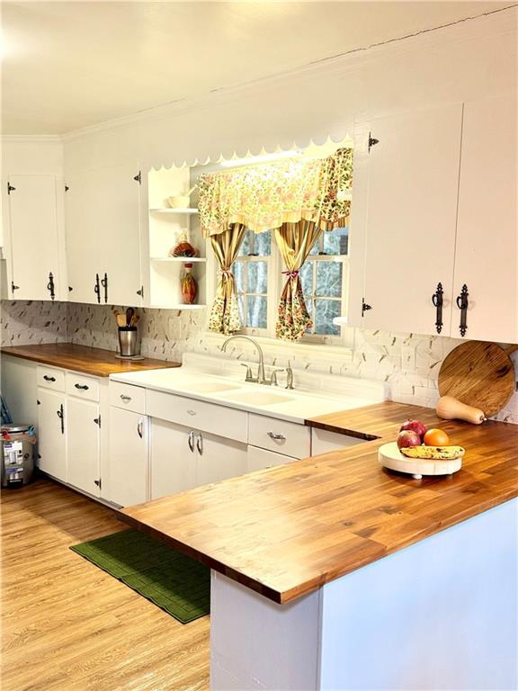 kitchen with white cabinetry, sink, wooden counters, and light hardwood / wood-style flooring