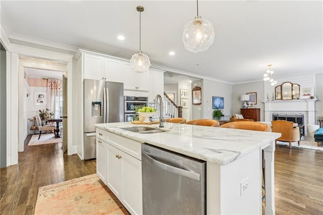 kitchen with light stone countertops, white cabinetry, appliances with stainless steel finishes, and a center island with sink