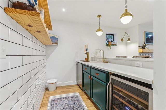 bar featuring pendant lighting, sink, green cabinets, light hardwood / wood-style floors, and beverage cooler