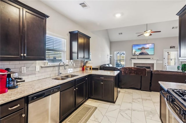 kitchen featuring a tile fireplace, sink, decorative backsplash, ceiling fan, and stainless steel appliances