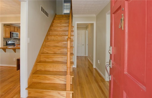 entryway with visible vents, light wood-style flooring, and crown molding