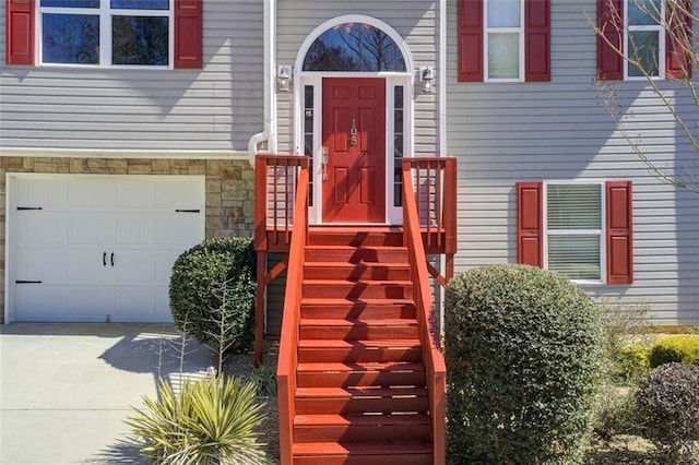 entrance to property with a garage, stone siding, and driveway