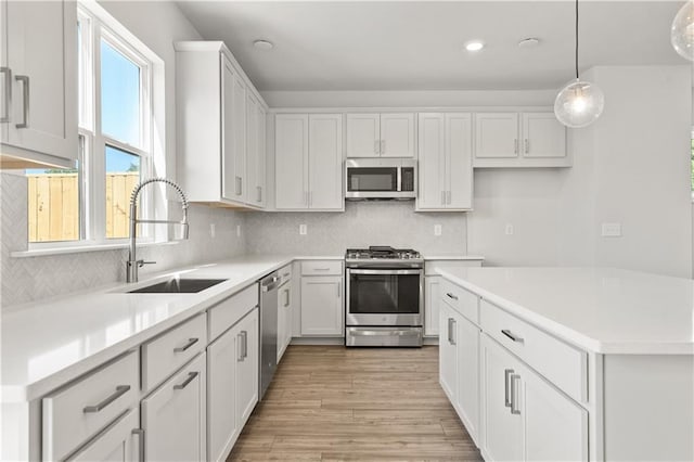 kitchen featuring sink, light hardwood / wood-style floors, white cabinetry, appliances with stainless steel finishes, and decorative light fixtures