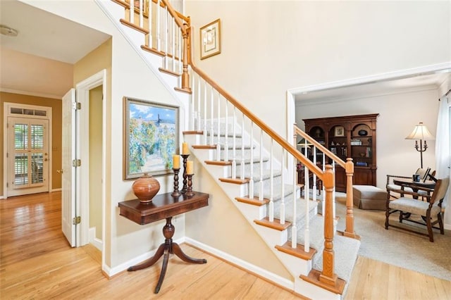 stairway with baseboards, wood finished floors, a towering ceiling, and ornamental molding