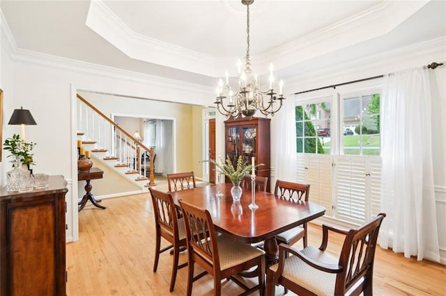 dining area with a chandelier, a raised ceiling, light wood-style floors, and stairs