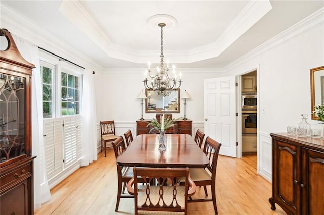 dining room with light wood-style floors, a chandelier, a raised ceiling, and crown molding