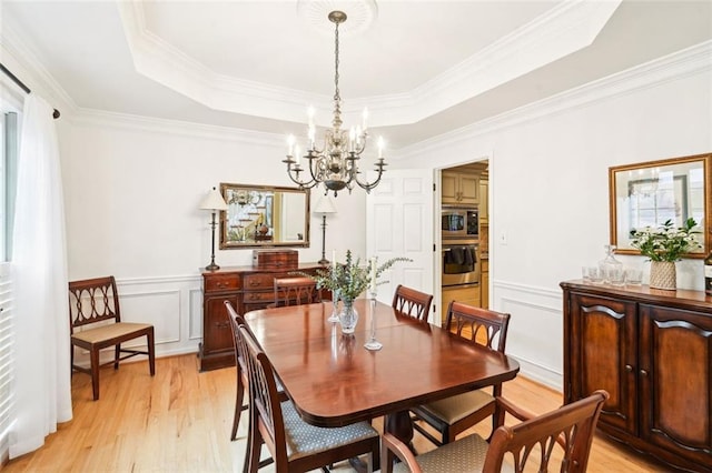 dining space with light wood-type flooring, a tray ceiling, a chandelier, and a decorative wall