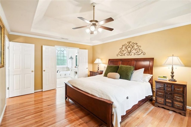 bedroom with light wood-style flooring, a tray ceiling, baseboards, crown molding, and connected bathroom